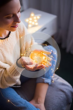 Pretty young woman in sweater holding glowing garland indoor