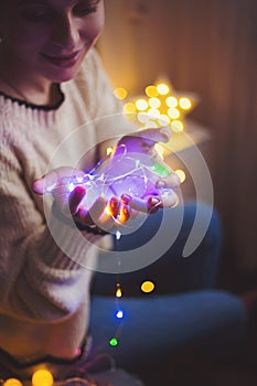 Pretty young woman in sweater holding glowing garland indoor