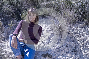 Pretty young woman in sweater sitting on a rock with nature park in background