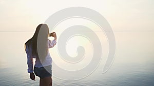 Pretty young woman taking pictures with her smartphone at sunset on the beach near the sea on vacation. slow motion