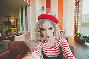 Pretty young woman taking selfie in cafe on blurred background