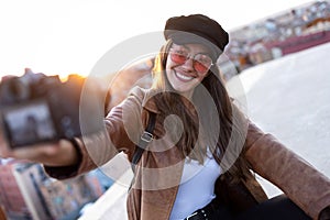 Pretty young woman taking a selfie with camera while sitting on the rooftop
