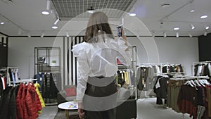 Pretty young woman is taking a selfie dressed in white shirt and black trousers at clothing store, tracking shot, 360