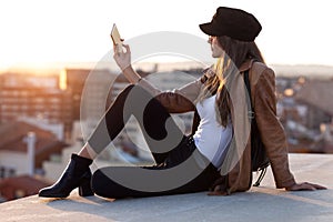 Pretty young woman taking a selfie with mobile phone while sitting on the rooftop