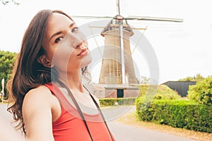 Pretty young woman taking selfie with an old dutch windmill