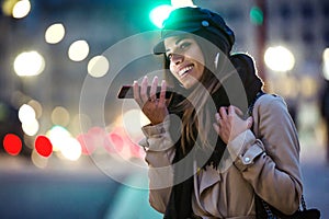 Pretty young woman talking with hands free of mobile phone in the street at night