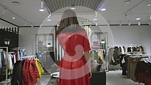 Pretty young woman is talking on her smartphone dressed in red dress at clothing store, tracking shot, 360 degree
