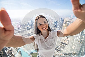 Pretty young woman tourist takes selfie portrait at the top of Burj Khalifa. Beautiful female student takes photo for travel blog