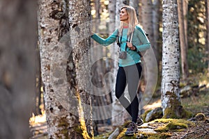 Pretty young woman traveler with backpack looking to the side while leaning on a tree in the natural forest