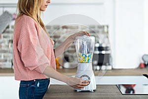 Pretty young woman using blender with diverse pills and capsules in the kitchen at home. Nutritional supplementation concept