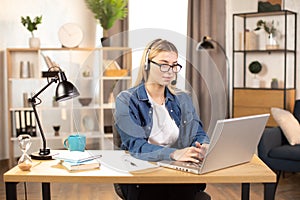 Pretty young woman using headset and laptop for video call, working at home