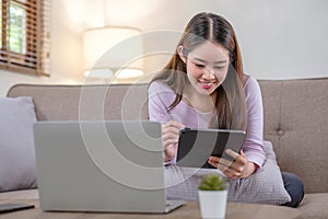 pretty young woman using her digital tablet for reading while sitting on sofa at home.