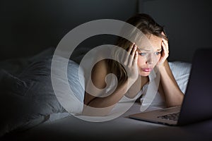Pretty, young woman using her laptop computer in bed