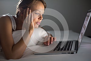 Pretty, young woman using her laptop computer in bed