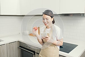 pretty young woman using her mobile phone while eating an apple in the kitchen at home