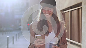Pretty young woman using her mobile phone while holding a coffee and standing in the street.