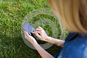 Pretty young woman using her mobile phone while lying on grass in the park.