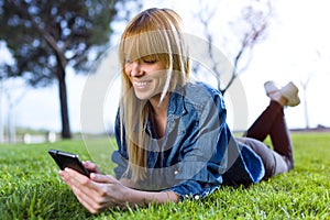 Pretty young woman using her mobile phone while lying on grass in the park.