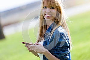 Pretty young woman using her mobile phone in the park.