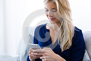 Pretty young woman using her mobile phone while sitting on sofa at home.