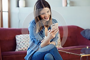 Pretty young woman using her mobile phone while sitting on sofa at home