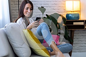 Pretty young woman using her mobile phone while sitting on sofa at home