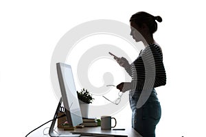 Pretty young woman using her mobile phone while standing in front of computer over white background