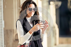 Pretty young woman using her mobile phone while standing in the street