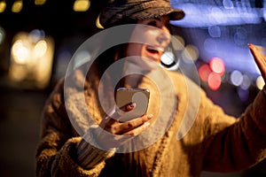 Pretty young woman using her mobile phone in the street at Christmas time