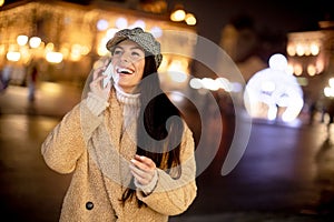Pretty young woman using her mobile phone in the street at Christmas time