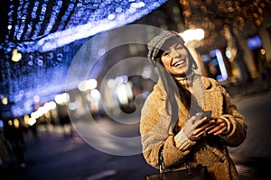 Pretty young woman using her mobile phone in the street at Christmas time