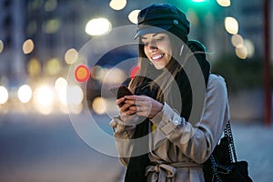 Pretty young woman using her mobile phone in the street at night