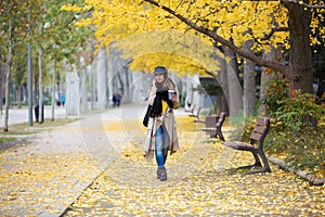 Pretty young woman using her mobile phone while walking through the park during autumn