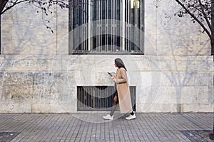 Pretty young woman using her mobile phone while walking in the street