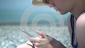 Pretty young woman using smartphone by the sea beach. Girl in retro hat and swimsuit with blue and white stripes