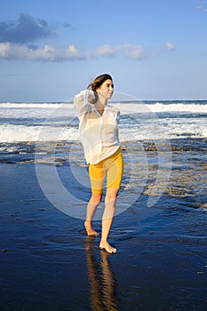 Pretty young woman walking on black sand beach. Caucasian woman wearing yellow sportswear and white blouse. Happiness and freedom