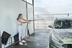 Pretty young woman washing her car in car wash station