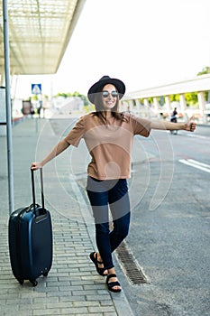 Pretty young woman waving with hand to catch a taxi at airport terminal