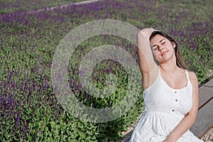 pretty young woman in white dress sitting at the sage flower field.