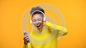 Pretty young woman in white headphones enjoying music sound on yellow background