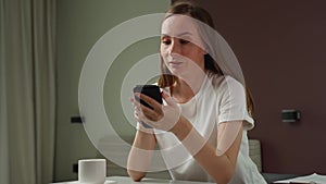 A pretty young woman in a white T-shirt uses a mobile smartphone, celebrating good news with a message, winning the