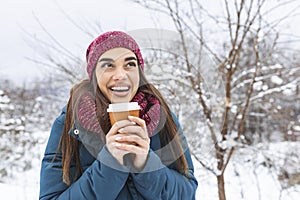 Pretty young woman in winter outfit holding disposable cup filled with hot coffee or tea. Girl holding mug of hot beverage in her