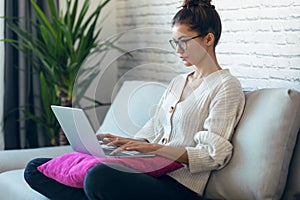 Pretty young woman working with her laptop while sitting on couch at home