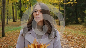 Pretty young women waiting for someone in the autumn park plaing with mapleleaf bouquet smile to someone