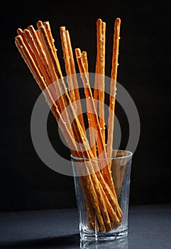 Pretzel sticks in small glass on black background photo