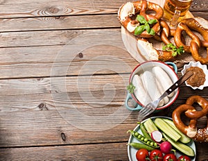 Pretzels, white bavarian sausages, beer and vegetables on old wooden background, german traditional food, oktoberfest