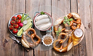 Pretzels, white bavarian sausages, beer and vegetables on wooden background, german traditional food, oktoberfest