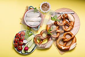 Pretzels, white bavarian sausages and vegetables on yellow background, german traditional food, oktoberfest