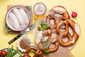 Pretzels, white bavarian sausages and vegetables on yellow background, german traditional food, oktoberfest