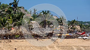 Pride flags in front of thatch roof beach bars and palapas on the beach